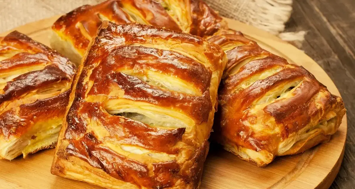 Złociste, pieczone ciasto francuskie z nadzieniem, ułożone na drewnianej desce.