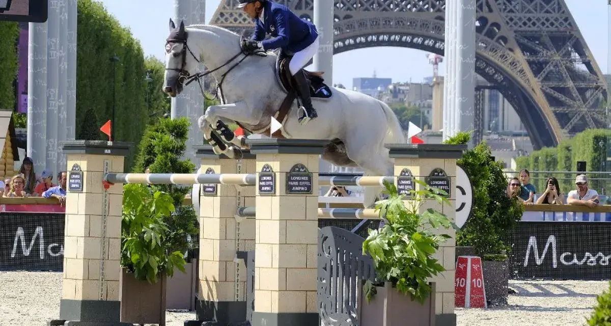 Un cavalier et son cheval blanc, Rahotep de Toscane, franchissent un obstacle à Paris, avec la Tour Eiffel en arrière-plan.
