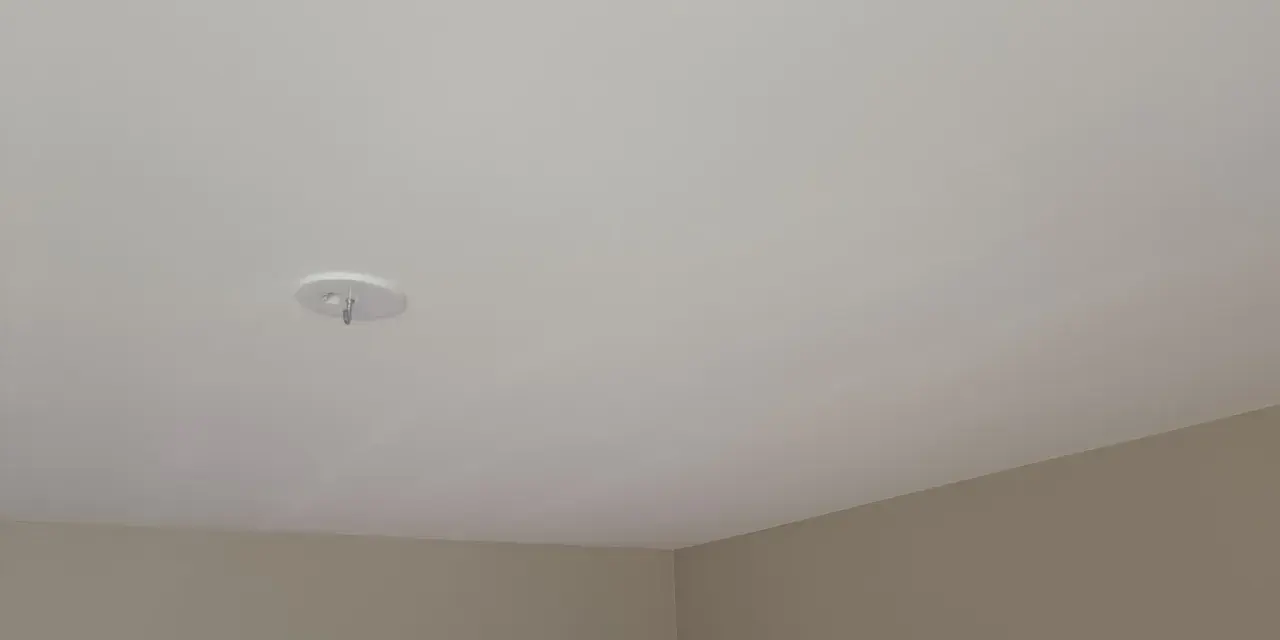Ett vitt tak med en krok för en lampa. Väggarna är ljusbruna. Snart dags att måla taket för en fräschare känsla.