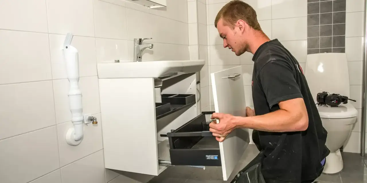 En rörmokare utför vvs arbeten i ett badrum, monterar ett nytt handfat och skåp.