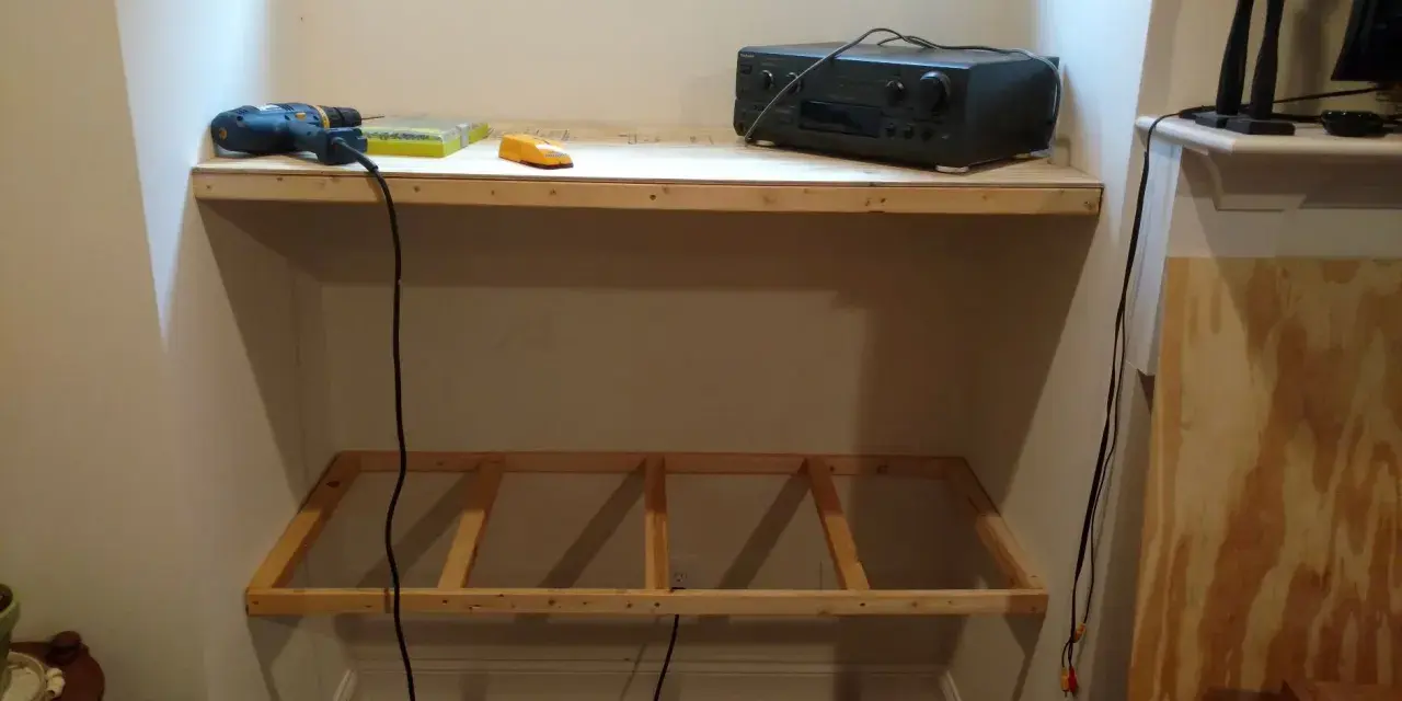 DIY project: a drill, screws, and audio receiver are on a shelf, with a wooden frame below, ready for how to hang shelves.