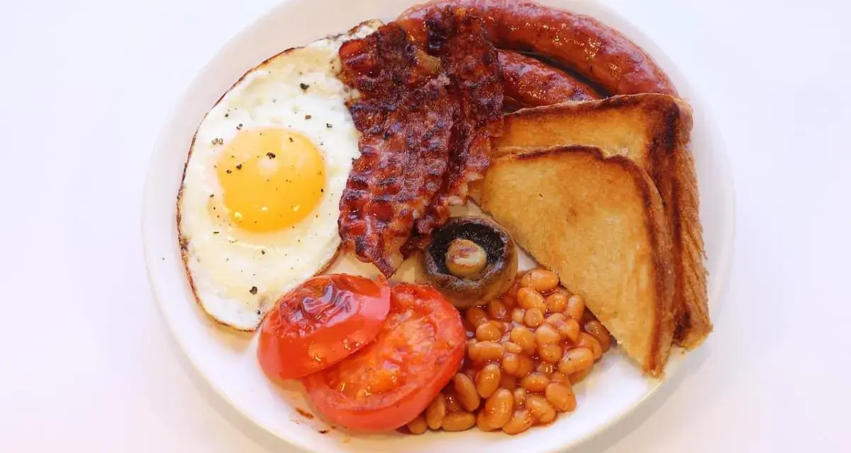 Un piatto tipico inglese con uovo fritto, bacon croccante, salsiccia, fagioli stufati, pomodori grigliati, fungo e toast.
