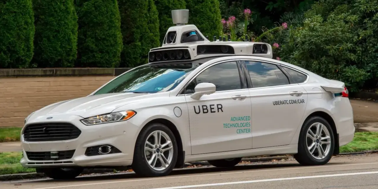 Ein weißes Uber auto mit Sensoren auf dem Dach fährt auf einer Straße.