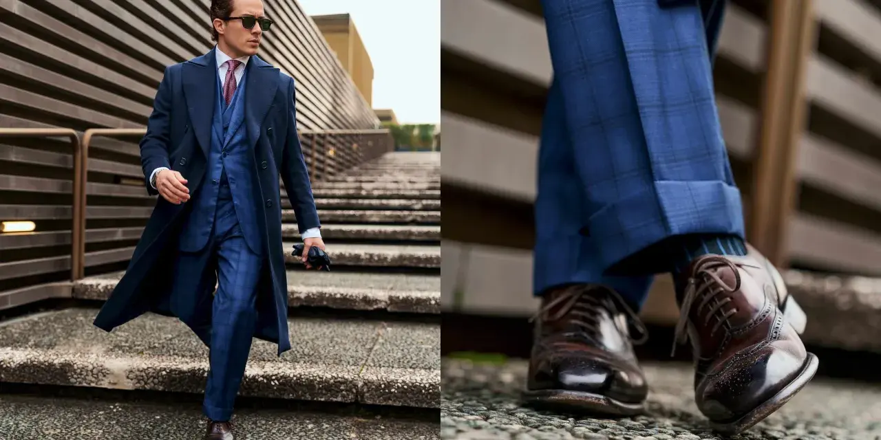 Un giovane uomo con un completo blu a quadri, cappotto scuro e occhiali da sole, cammina con passo sicuro. Un vero old money boy.