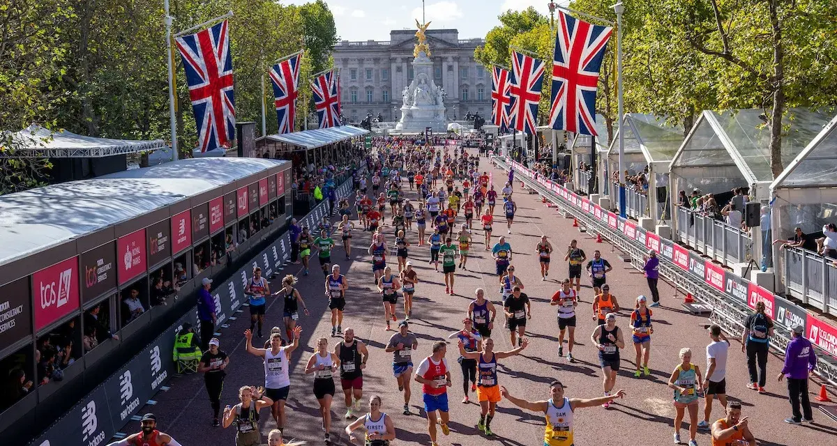 Tysiące biegaczy na trasie maratonu londyn, z flagami Wielkiej Brytanii i Pałacem Buckingham w tle.
