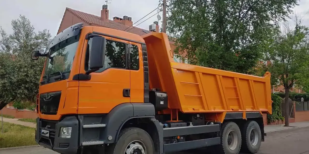 Pomarańczowa wywrotka, idealna do pracy dla posiadaczy prawa jazdy kat C. Gotowa do transportu materiałów budowlanych.