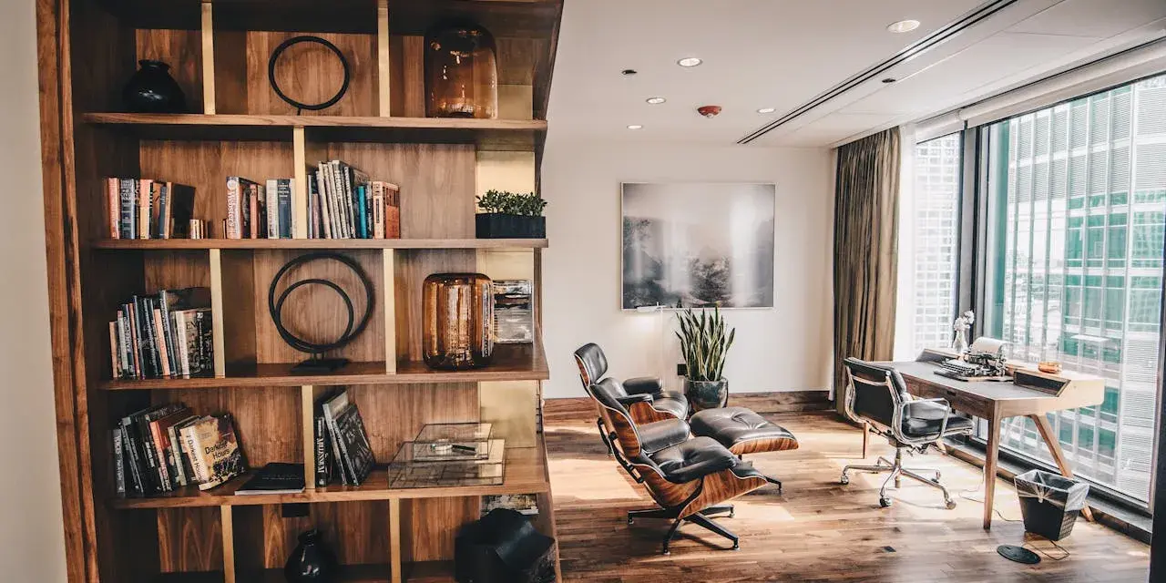 Drewniana biblioteczka z książkami i dekoracjami, obok skórzane fotele i biurko z maszyną do pisania. Styl **modern rustic**.