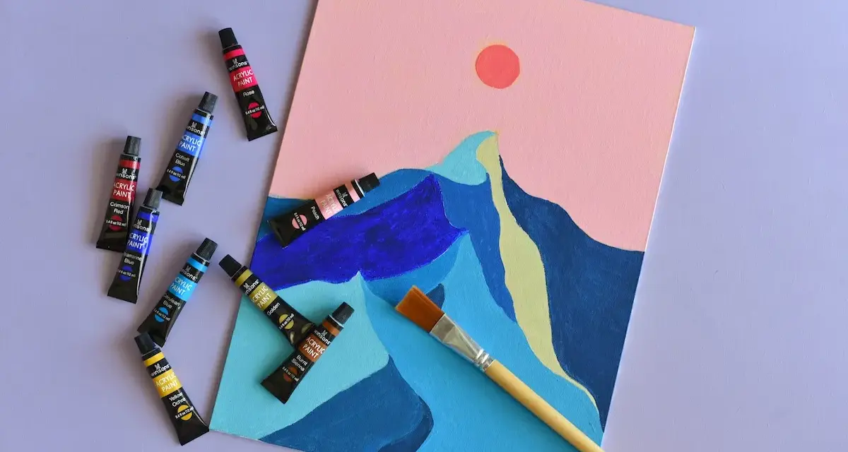 Des tubes de peinture acrylique et un pinceau sont disposés autour d'une toile représentant des montagnes stylisées sous un ciel rose. Une peinture à faire, prête à être créée.