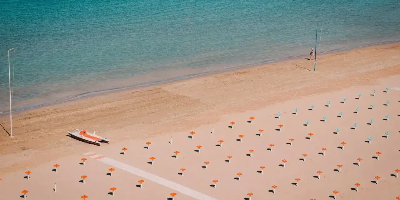 Pusta plaża w Rimini z rzędami pomarańczowych parasoli i łodzią ratowniczą.