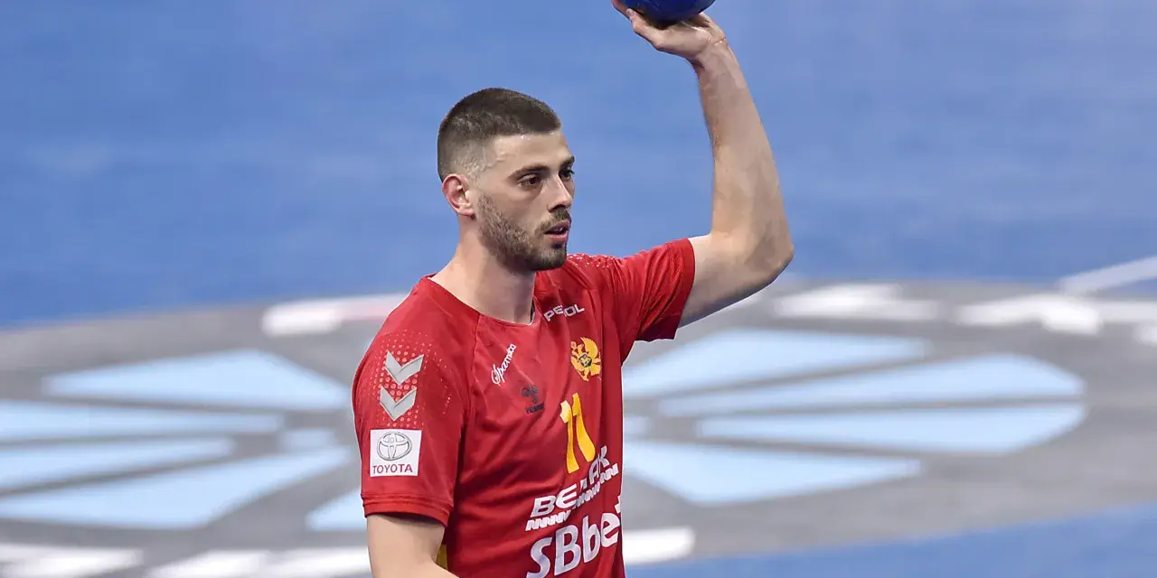 Branko Vujović, zawodnik piłki ręcznej, w czerwonej koszulce z numerem 11, trzyma piłkę nad głową.