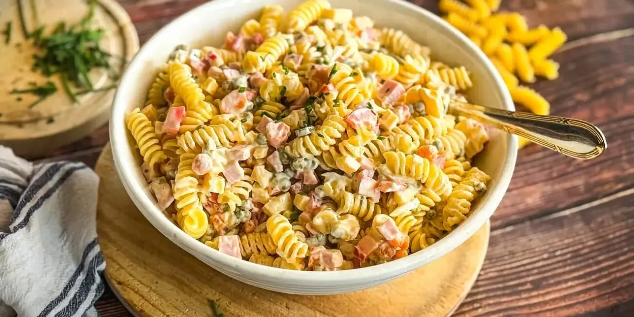 Cremiger Nudelsalat mit Schinken, Erbsen und einem leckeren Dressing, garniert mit frischen Kräutern.