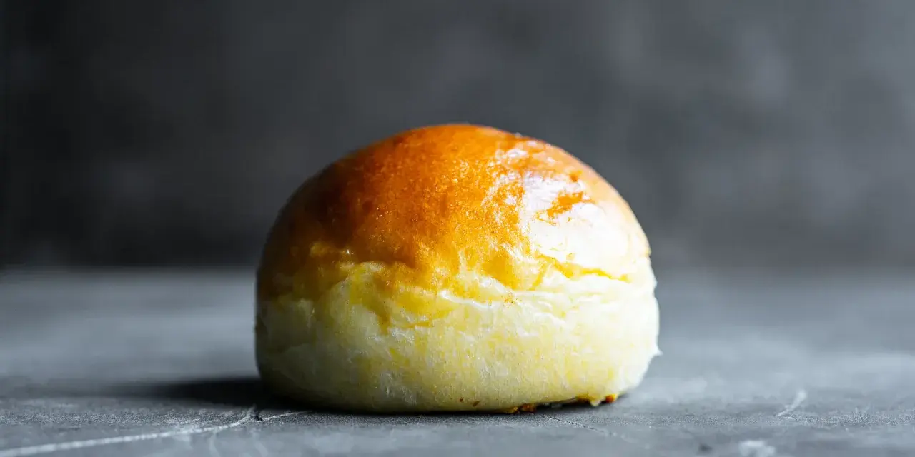 Ein goldbraunes Brioche-Brötchen liegt auf einer dunklen Oberfläche.