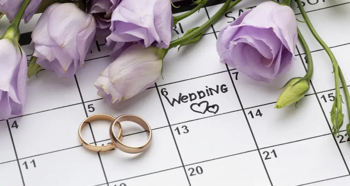 Anelli d'oro su un calendario segnato con "Wedding" e fiori lilla. Il giorno perfetto quando sposarsi.