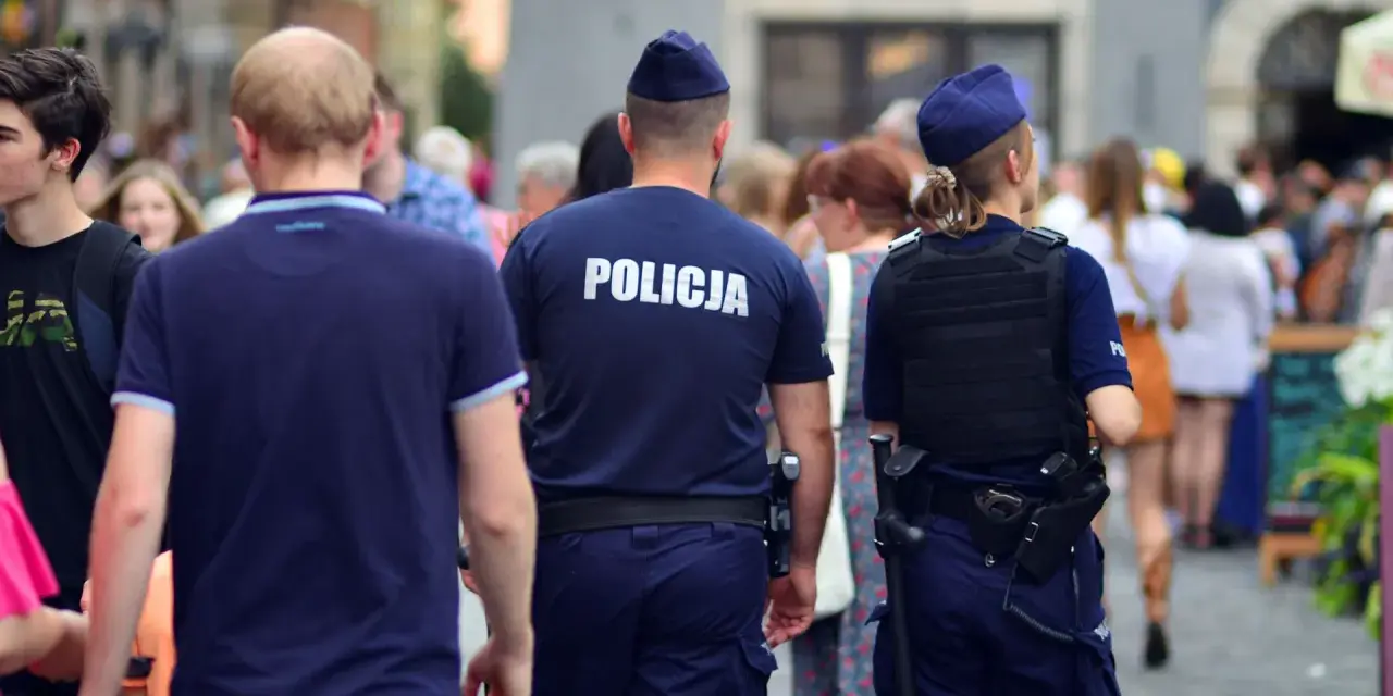 Policja w patrolu, kiedy policja szuka dłużnika. Dwóch funkcjonariuszy w mundurach idzie ulicą wśród tłumu ludzi.