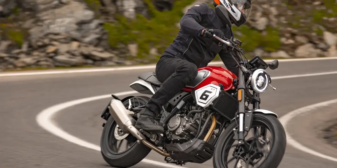 Motocyklista w kasku jedzie czerwonym motocyklem po krętej drodze. Idealny motocykl na początek przygody z jazdą.