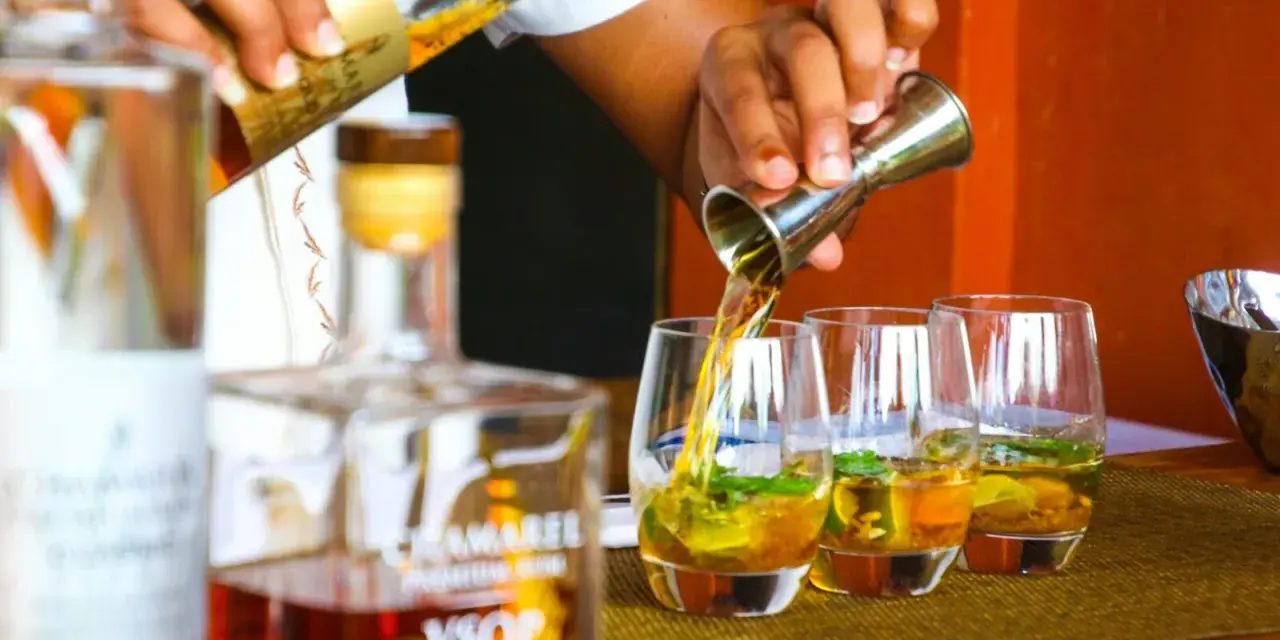 Ein Barkeeper gießt bernsteinfarbenen Rum in Gläser mit Eis und Minze. Die Frage "ab wann brennt Schnaps" wird hier durch das Servieren von edlem Rum beantwortet.
