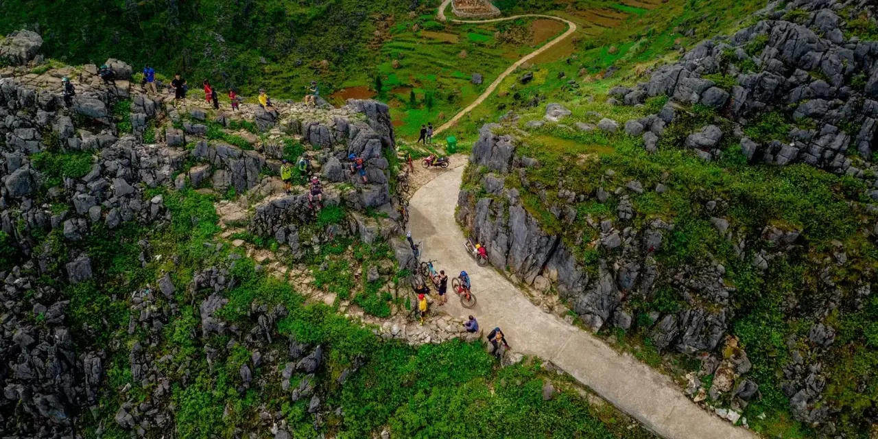 Grupa rowerzystów na malowniczej trasie Ha Giang Loop, wśród skalistych zboczy i zielonych tarasów.