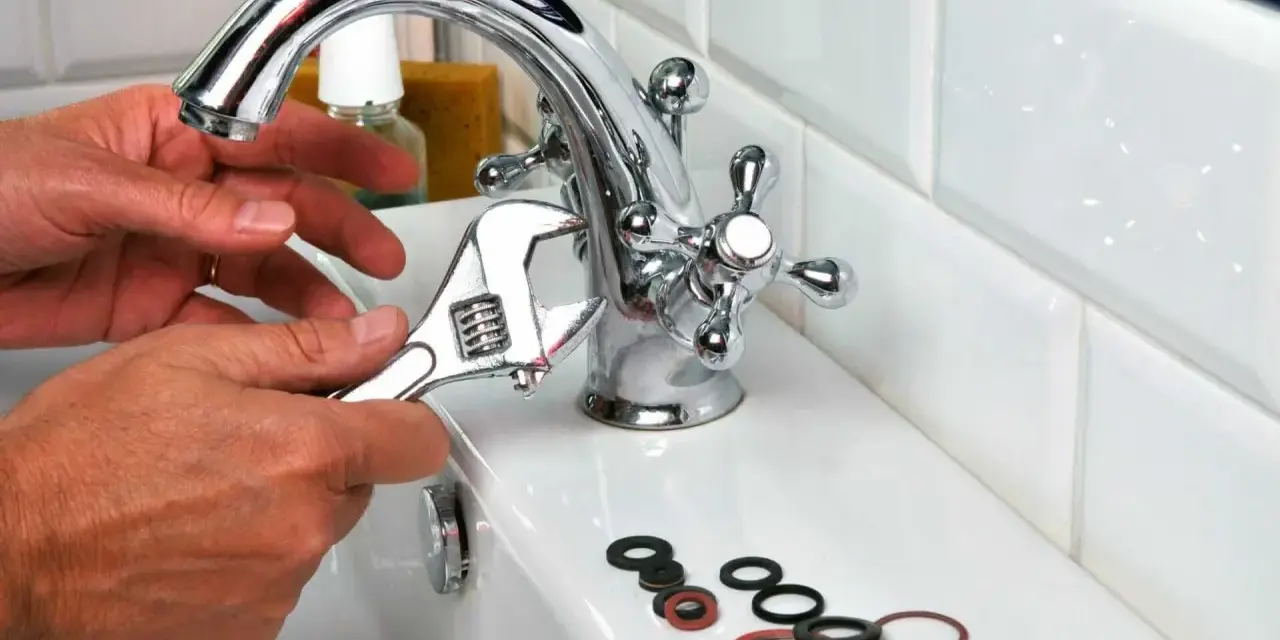 Main tenant utilise une clé pour changer un joint de robinet. Des joints sont posés sur le lavabo.