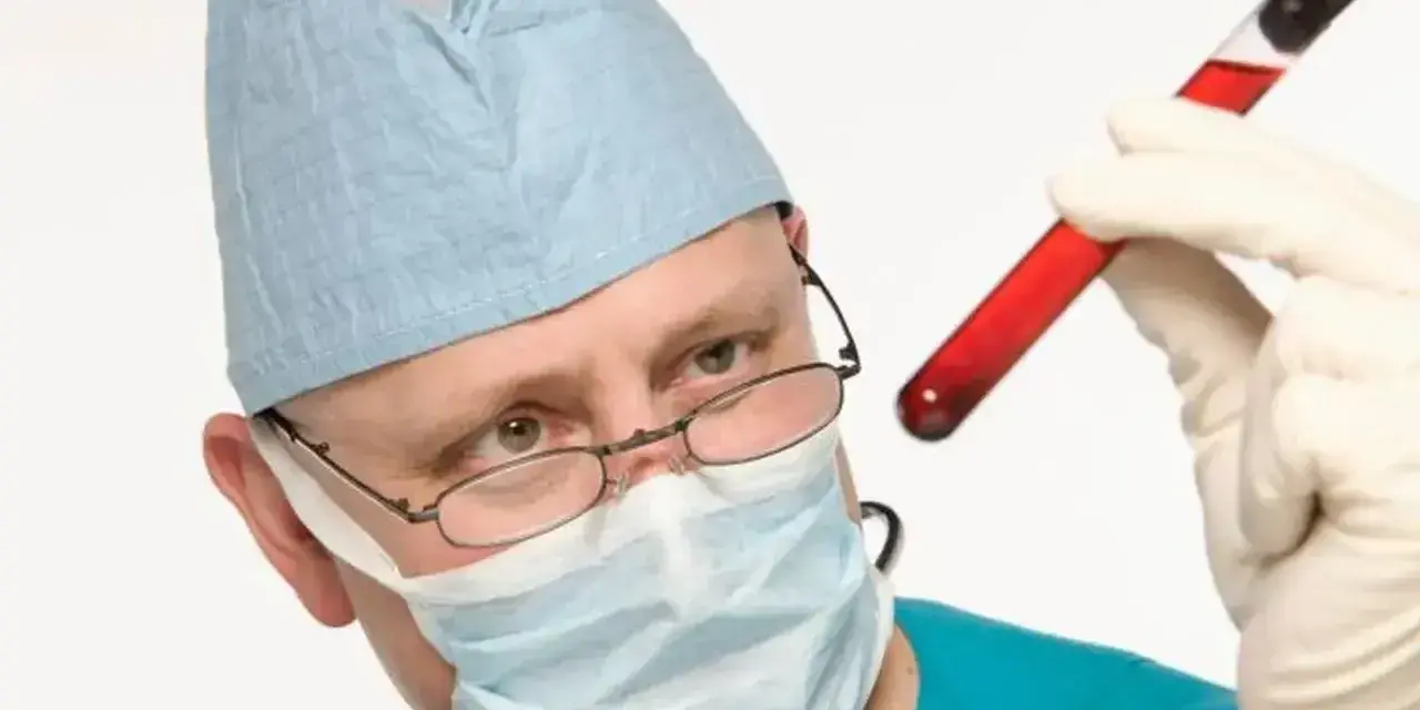 Medyk w masce i czepku ogląda probówkę z krwią. Badanie krwi to ważny element diagnostyki.