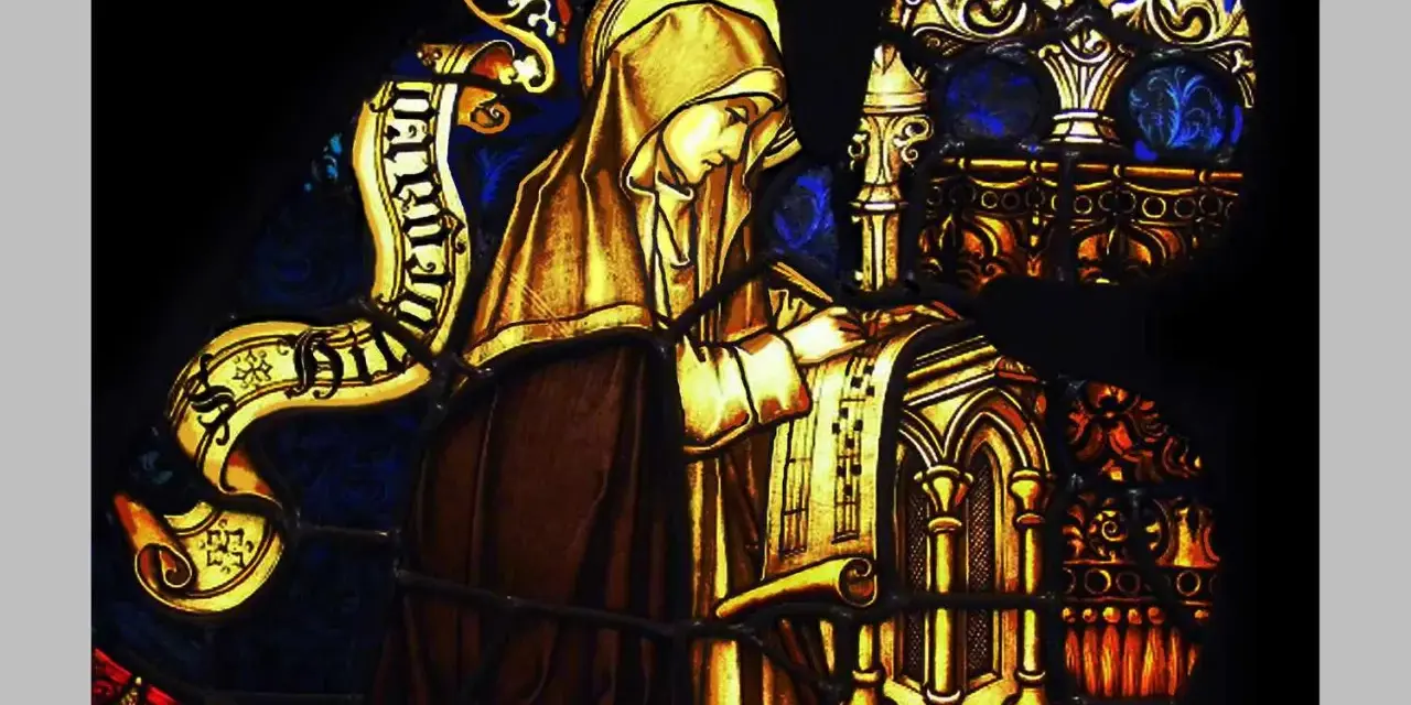Stained glass depicts a cloaked figure, likely the head of a monastery, diligently writing on a scroll.