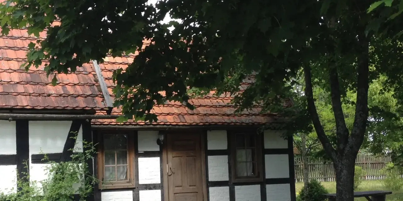 Urokliwa chata kaszubska z drewnianymi belkami i czerwoną dachówką, otoczona zielenią.