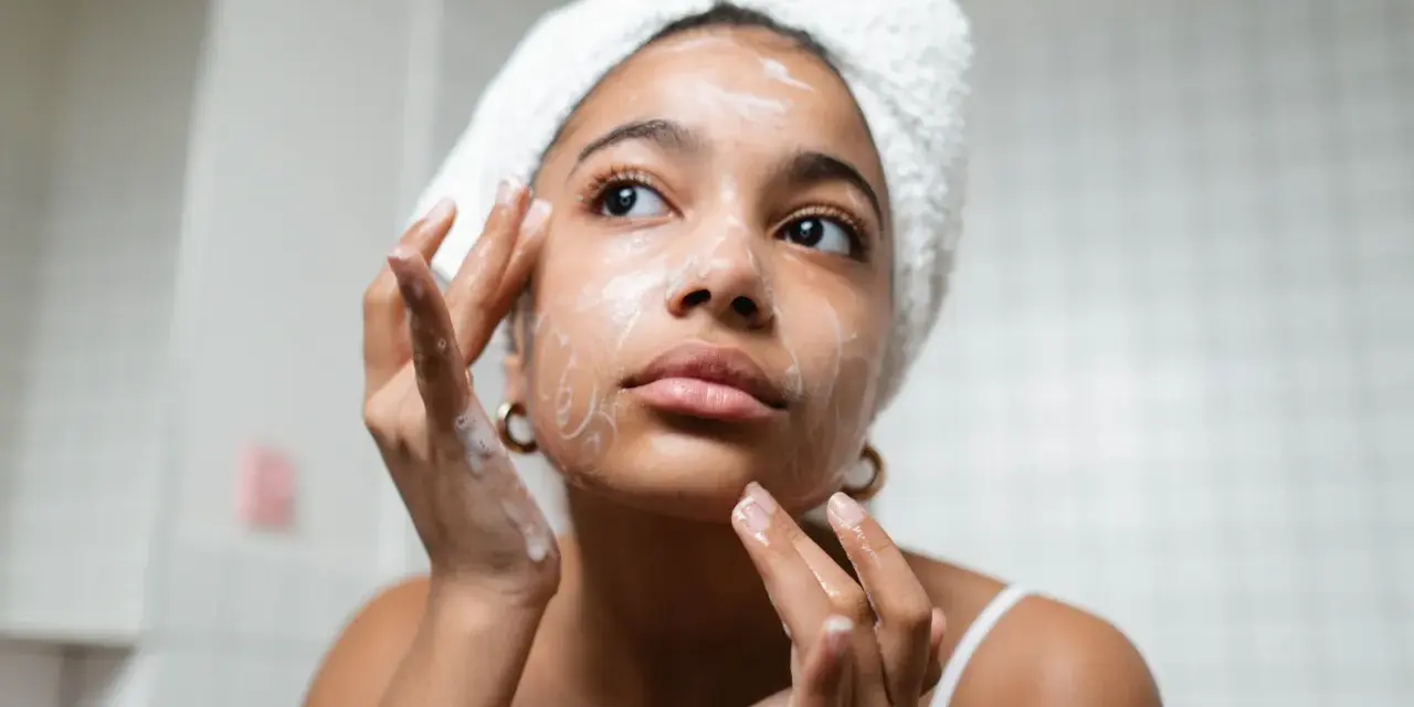 Rutina de limpieza facial: mujer con toalla en la cabeza aplica espuma en su rostro, un paso esencial para como cuidar mi piel.
