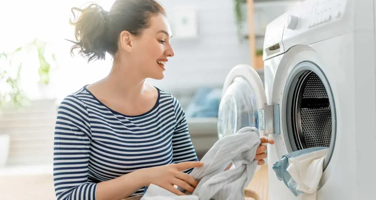 Donna sorridente carica la lavatrice, mostrando il funzionamento di un elettrodomestico moderno per il bucato.
