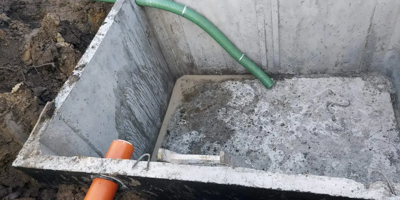Szambo betonowe 10m3 cena z montażem. Instalacja wkopana w ziemię, widoczne rury doprowadzające.
