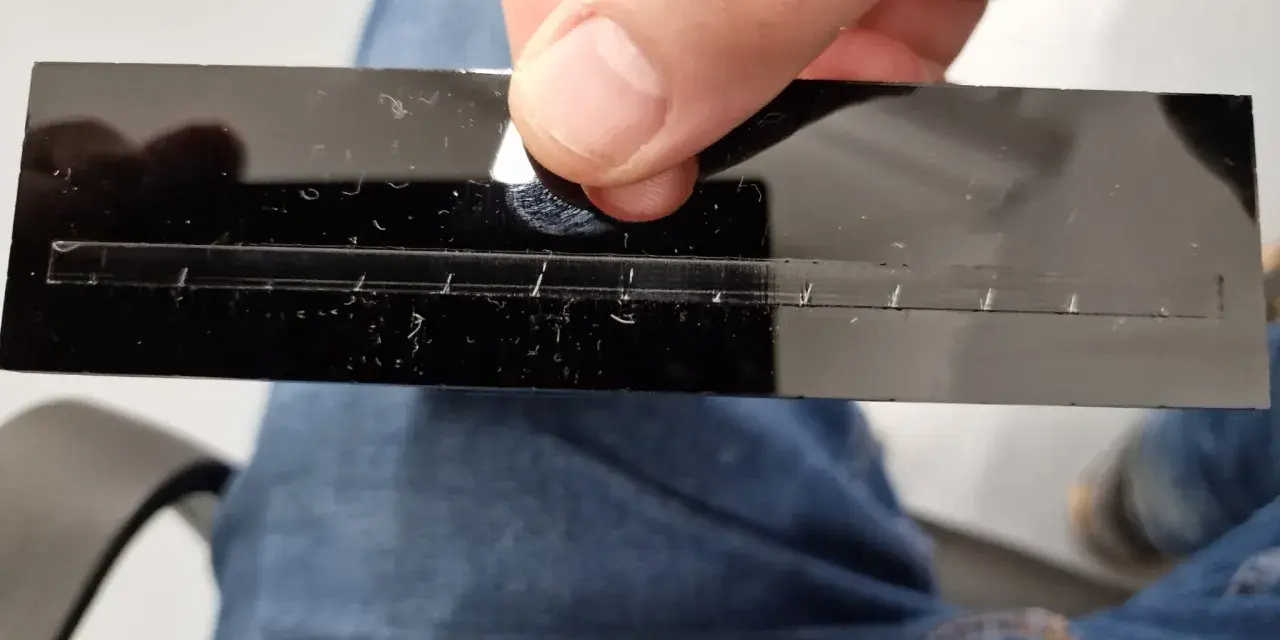 A hand holds a black acrylic strip with a precisely cut slot, demonstrating how to laser cut acrylic at home.