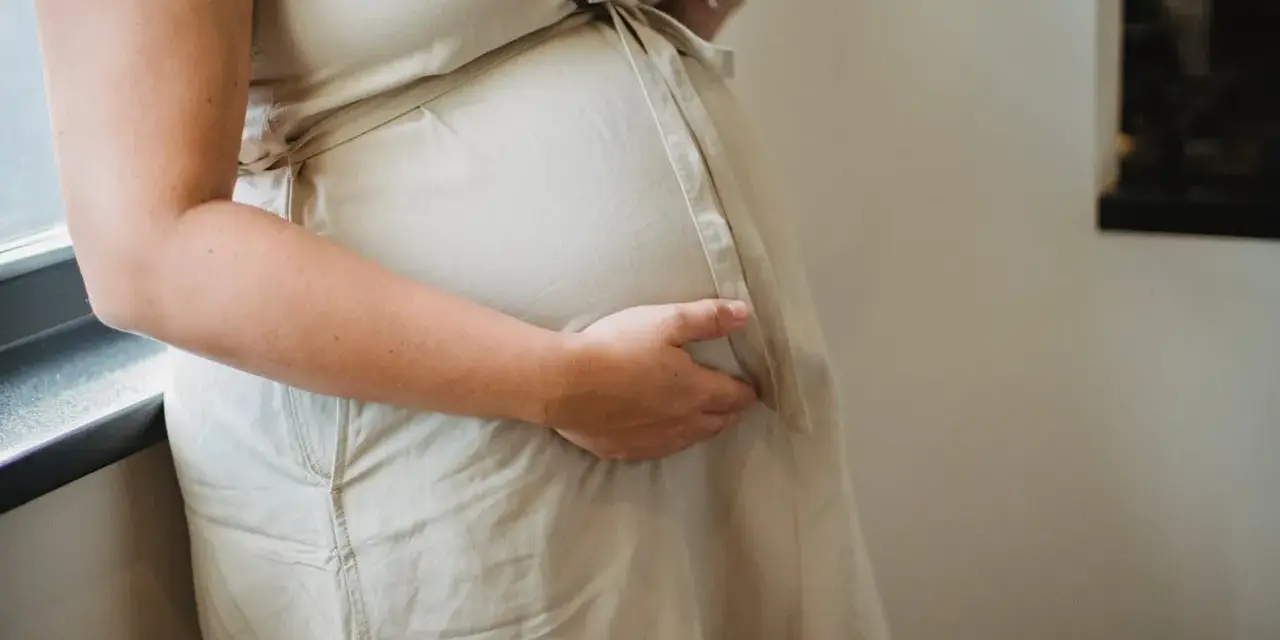 Ciężarna kobieta w beżowej sukience, która dba o zdrowie swoje i dziecka, rozważa suplementację: olej lniany w ciąży.