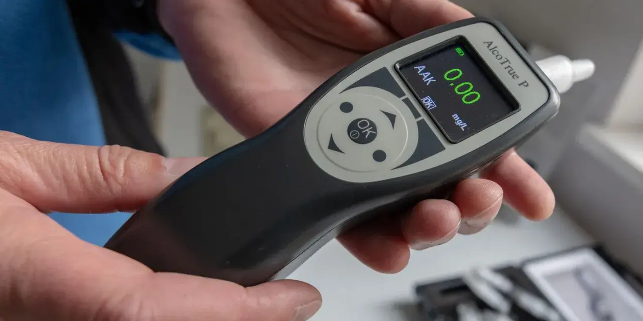 Hände halten ein Alkoholtestgerät, das 0.00 mg/L anzeigt. So vermeidet man eine Strafe wegen Alkohol am Steuer.