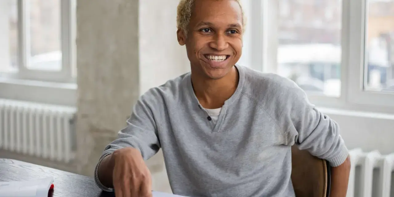 Lächelnder Mann mit blonden Haaren sitzt am Schreibtisch, Notizbuch und Stift bereit für sein Praktikum in Deutschland.
