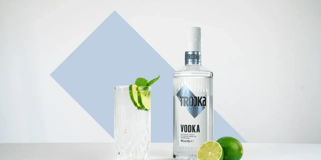 Ein Glas mit Eis, Limette und Minze steht neben einer Flasche Trojka Wodka. Perfekt für einen erfrischenden Wodka mit Wasser.