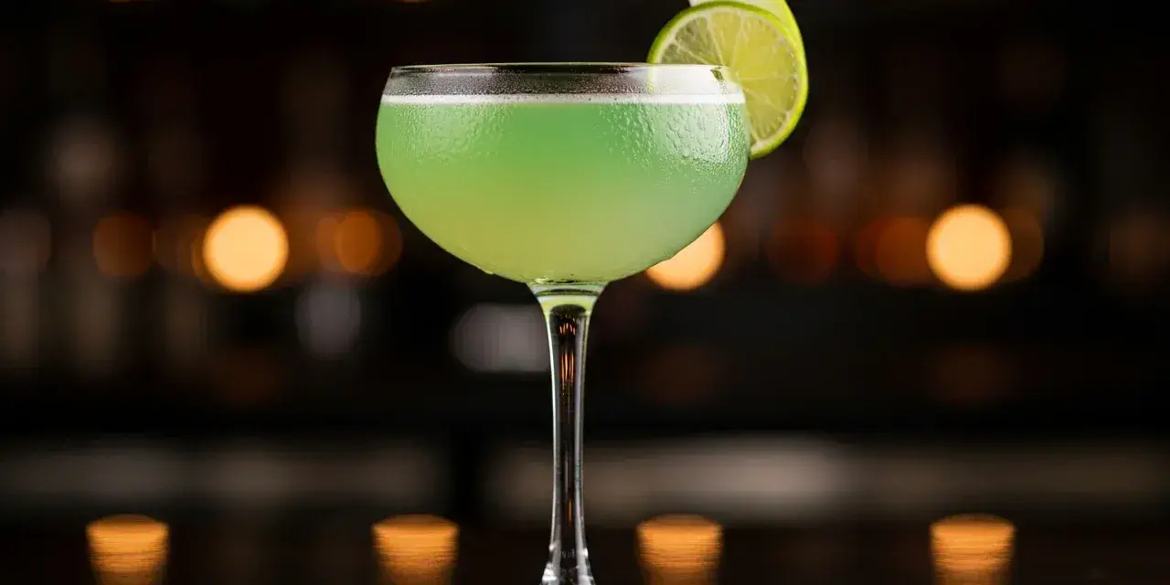 En grön, uppfriskande p2 drink med lime och äpple som garnityr, serverad i ett elegant glas mot en mjukt belyst bakgrund.