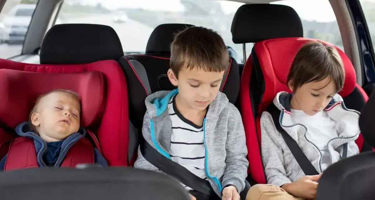 Dzieci w fotelikach samochodowych. Maluch śpi, starsi grają na telefonach. Zastanawiasz się, od jakiego wzrostu bez fotelika można podróżować?