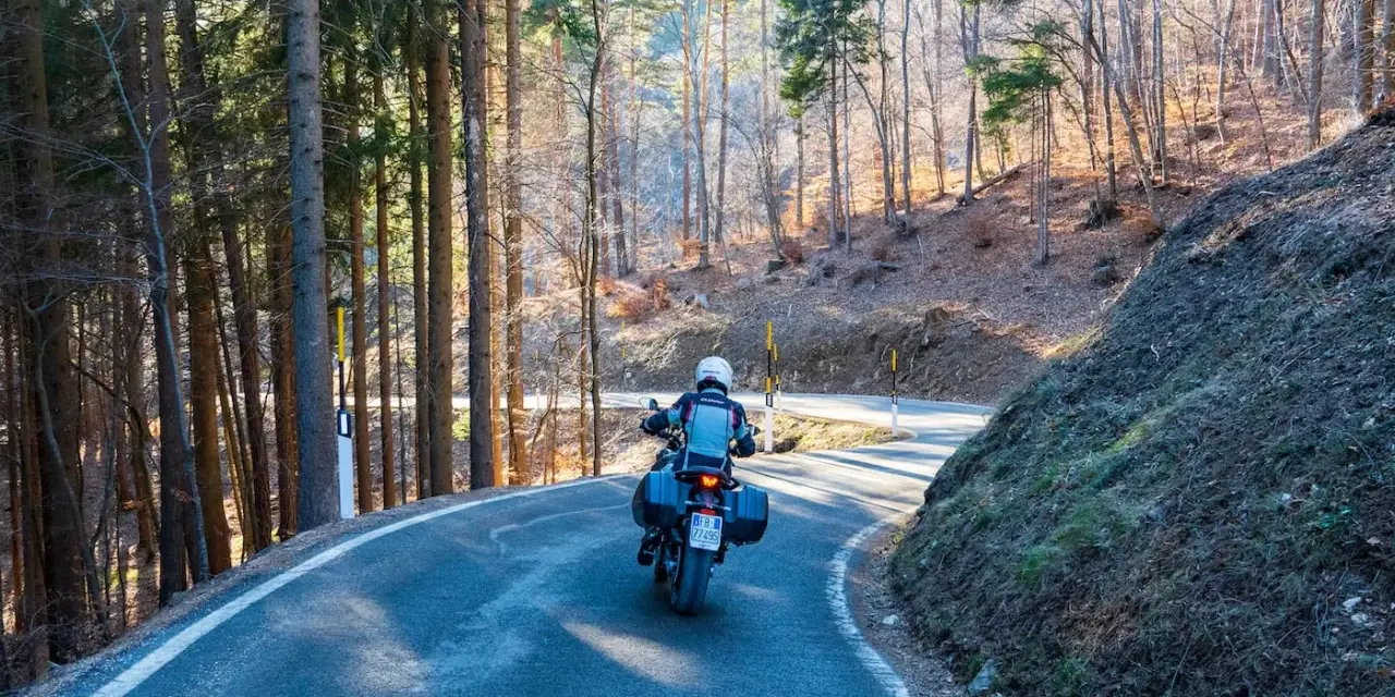 Motociclista su strada tortuosa tra i boschi, un'avventura **rund um den Gardasee**.