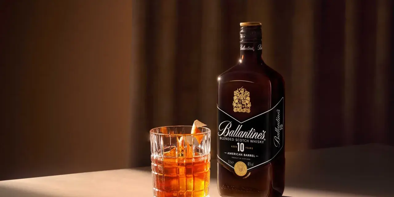 Elegancki drink Rob Roy z whisky Ballantine's 10 Year Old, podany w szkle z lodem i skórką pomarańczy.