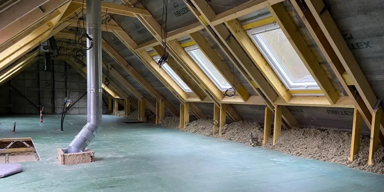 Aménagement des combles d'une maison Phénix : charpente, fenêtres de toit, isolation et gaine de ventilation en cours.