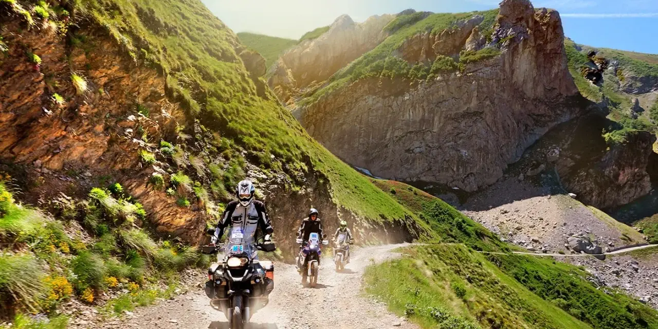 Un gruppo di motociclisti affronta un emozionante giro in moto in Liguria, su una strada sterrata tra montagne verdi e rocce imponenti.