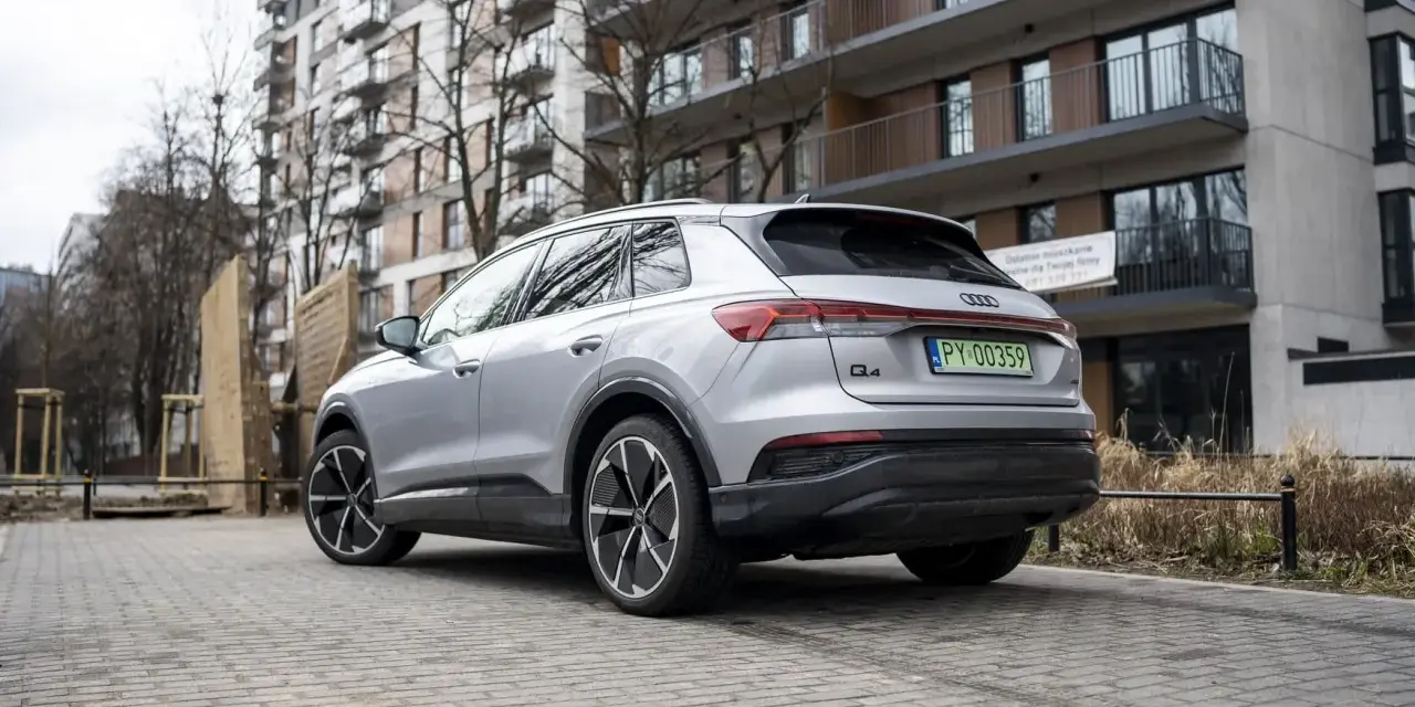 Srebrny Audi Q4 e-tron zaparkowany przed nowoczesnym budynkiem mieszkalnym.