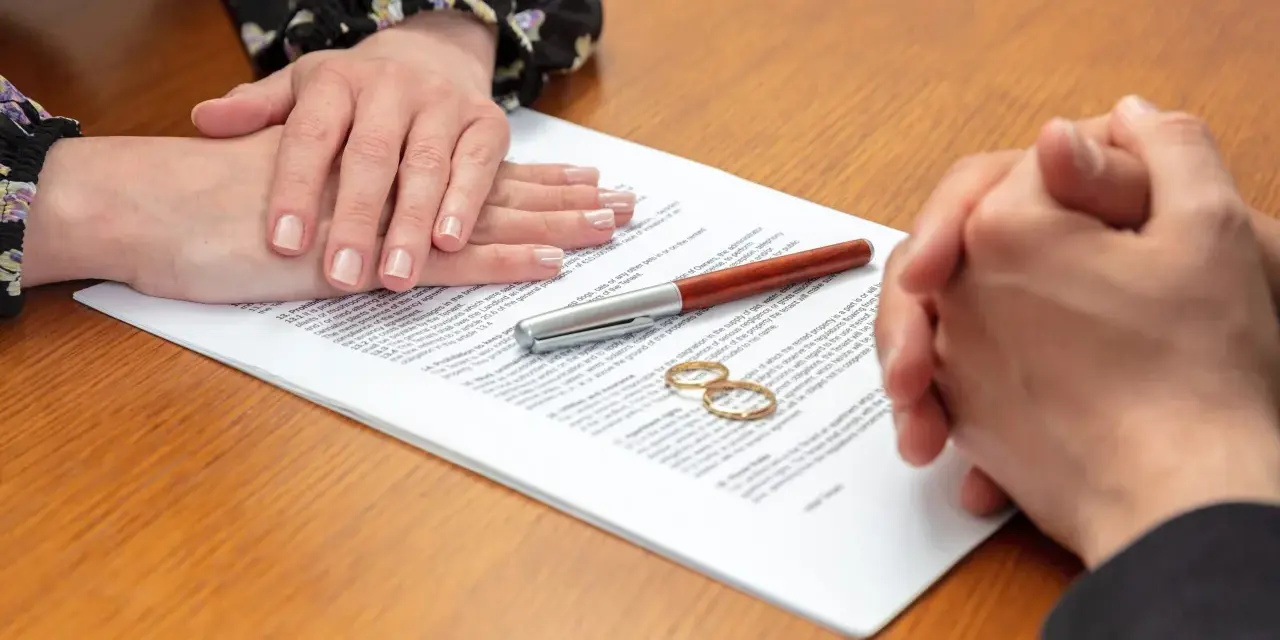 Deux mains se serrent au-dessus d'un contrat, deux alliances posées sur le document. Qui demande le plus le divorce ?