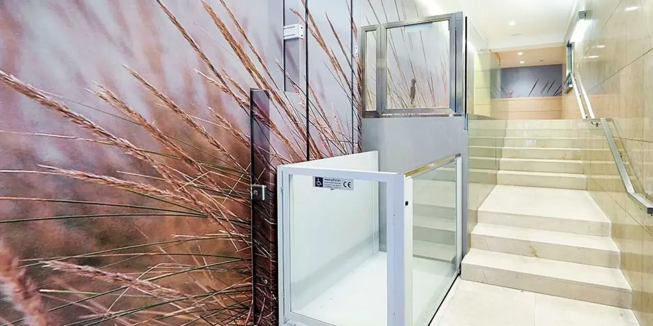 Un portal de vecinos moderno con un mural de hierbas secas y una plataforma elevadora de cristal.
