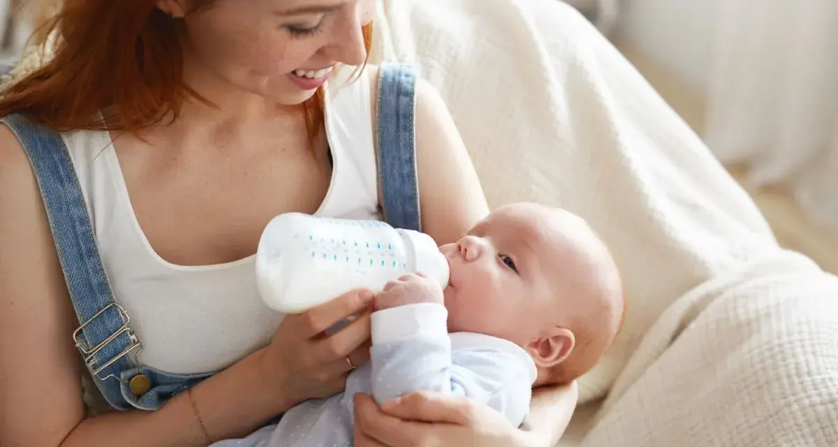 Uśmiechnięta mama karmi piersią swoje dziecko z butelki, szukając najlepszych butelek dla noworodka.