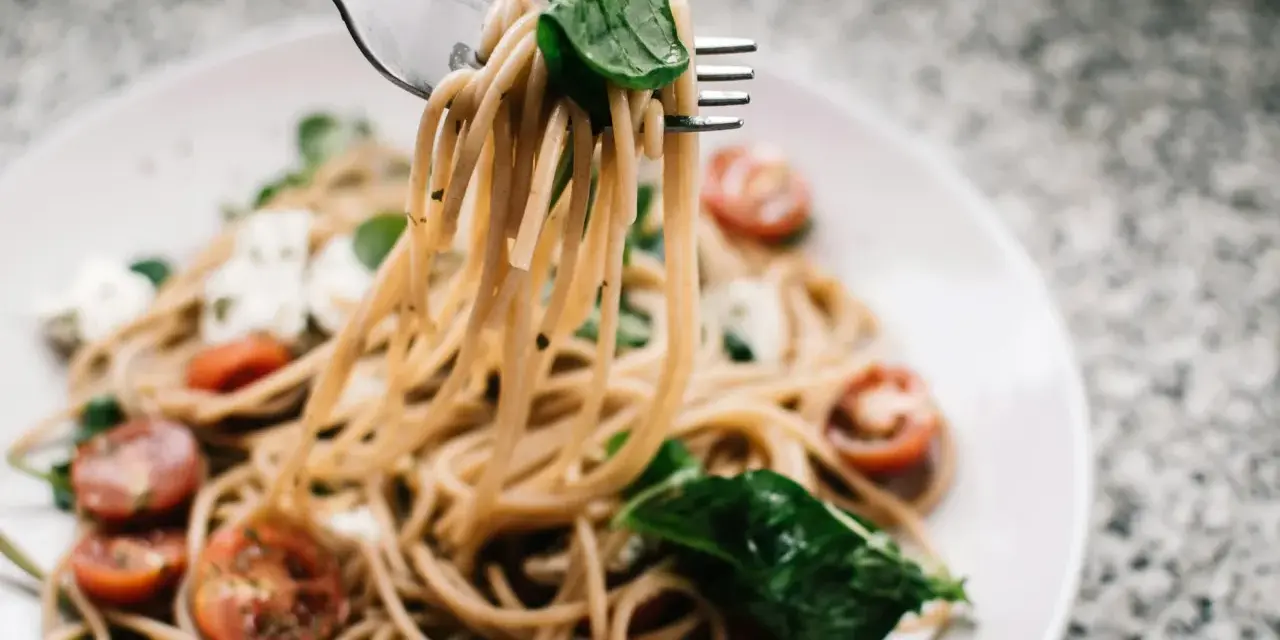 Widelec podnosi porcję spaghetti z pomidorkami i mozzarellą. Czy makaron to węglowodany? Tak, to pyszne źródło energii!