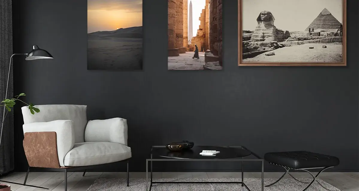 Trois tableaux sur un mur sombre : un coucher de soleil sur les dunes, une personne marchant dans un temple égyptien, et le Sphinx et les pyramides. La **couleur référence** de la pièce est le gris anthracite.