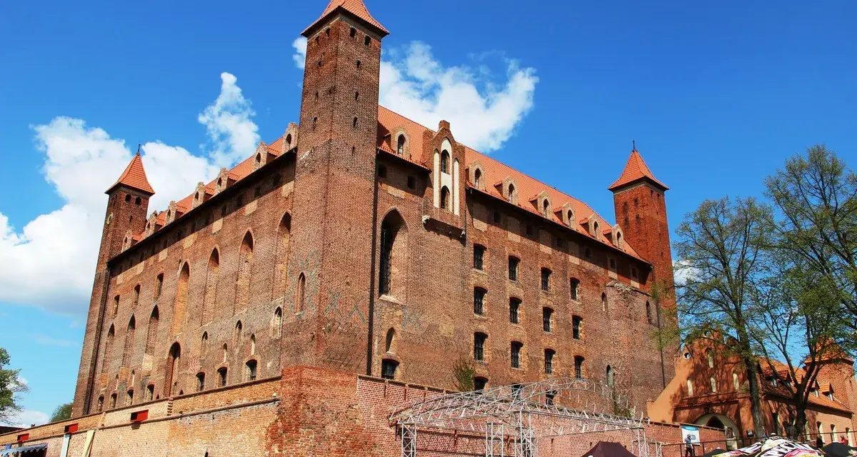 Potężny zamek w Gniewie, ceglana twierdza z wieżami i czerwonymi dachami, pod błękitnym niebem. Ciekawostki o jego historii czekają na odkrycie.
