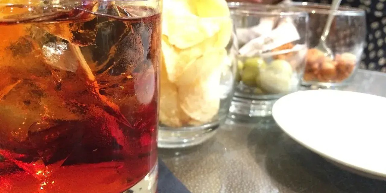 Orzeźwiający drink z lodem i cytryną, obok chipsy i oliwki. Idealne połączenie, by dowiedzieć się, **sambuca z czym pić**.