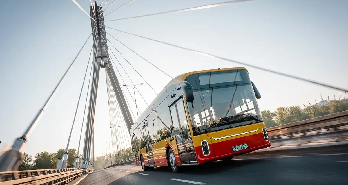 Żółto-czerwony autobus elektryczny Yutong U12 jedzie po moście nad rzeką.