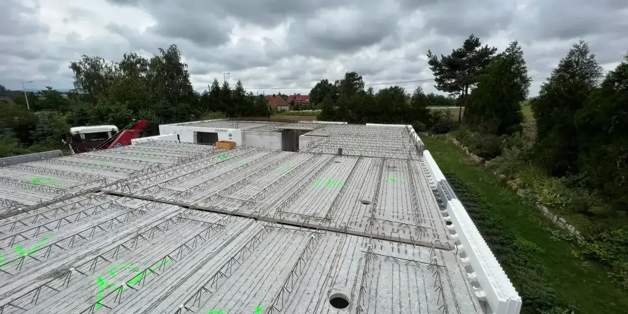 Gotowy do wylania strop, zbrojenie czeka na beton. W tle drzewa i pochmurne niebo.