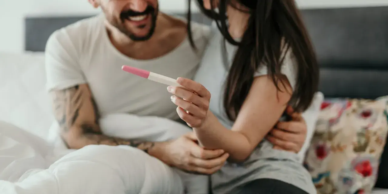 Ein Paar hält einen Schwangerschaftstest, der positiv ist. Was zeigt ein Ovulationstest an, wenn man schwanger ist? Zwei rosa Linien.